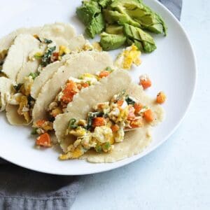 Sweet potato and spinach breakfast tacos on a white place with avocado slices on the side.