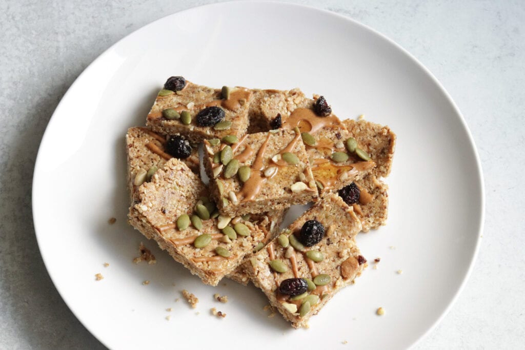 Cashew Everything Bars topped with pumpkin seeds, raisins, nuts, and local Two Hives honey on a white plate.