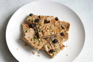 Cashew Everything Bars topped with pumpkin seeds, raisins, and nuts on a white plate.