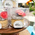 Dolce Terra mini buttercream cakes with fresh flowers packaged in clear boxes on a wooden cake stand.